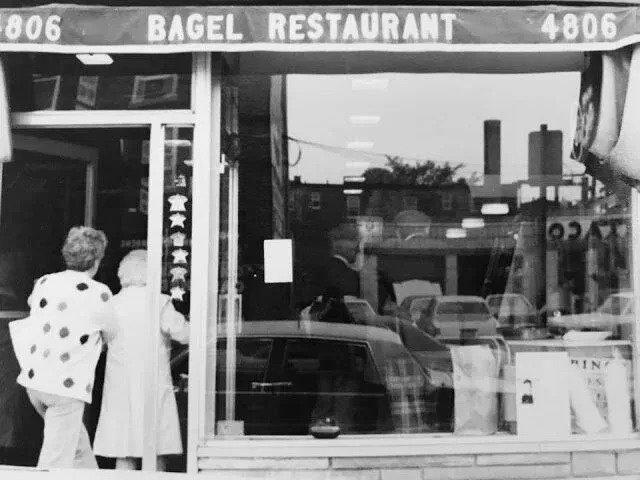 Black-and-white photo of two women entering a storefront under a Bagel Restaurant awning marked 4806