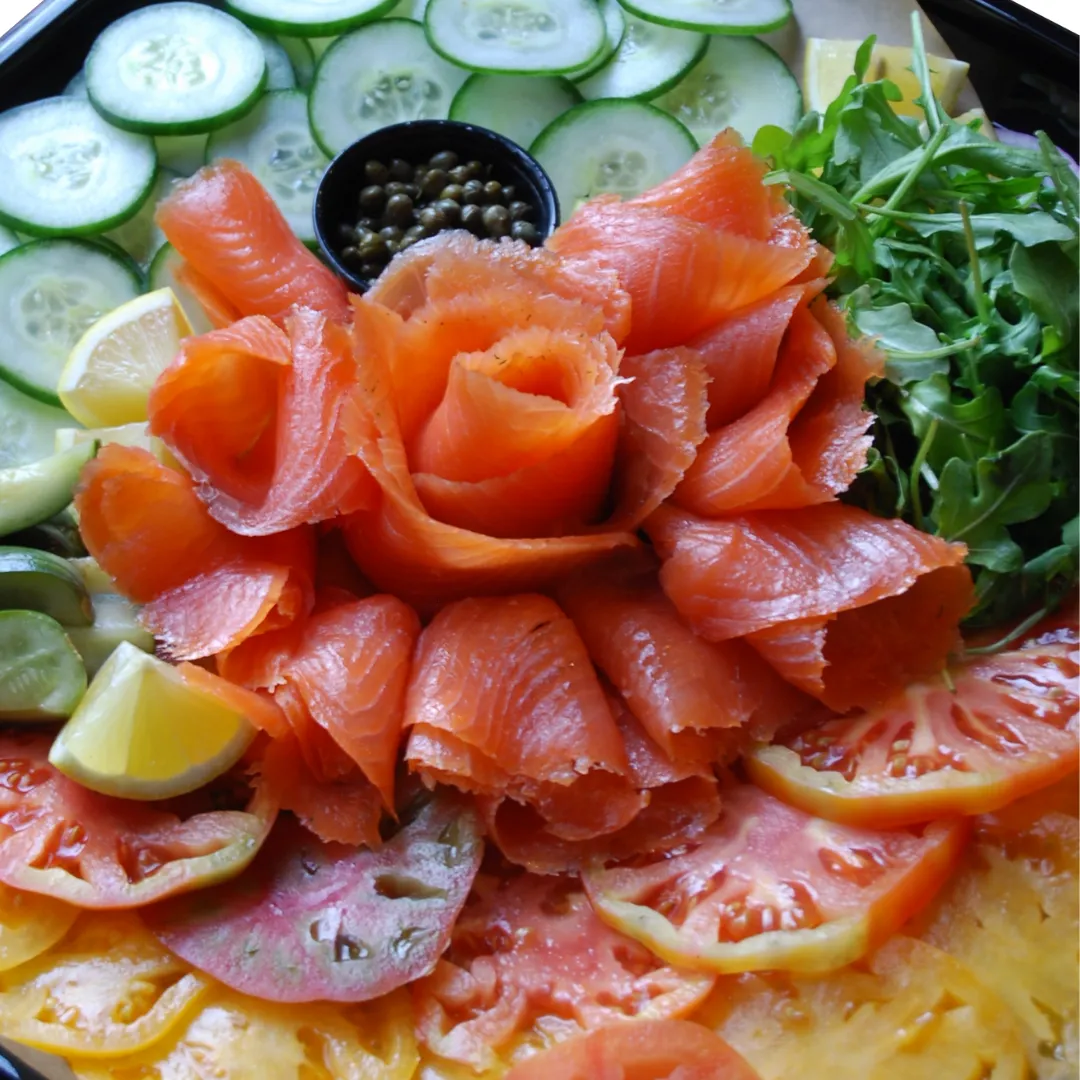 Platter of smoked salmon ribbons with cucumber slices, capers, lemon wedges, arugula and sliced tomatoes