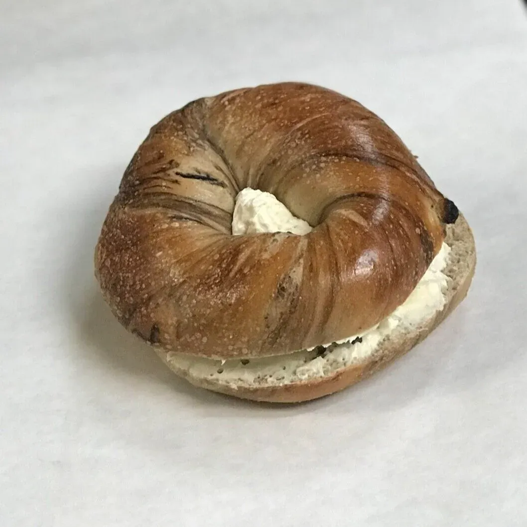 Cinnamon raisin bagel sliced and filled with a thick layer of cream cheese on white parchment