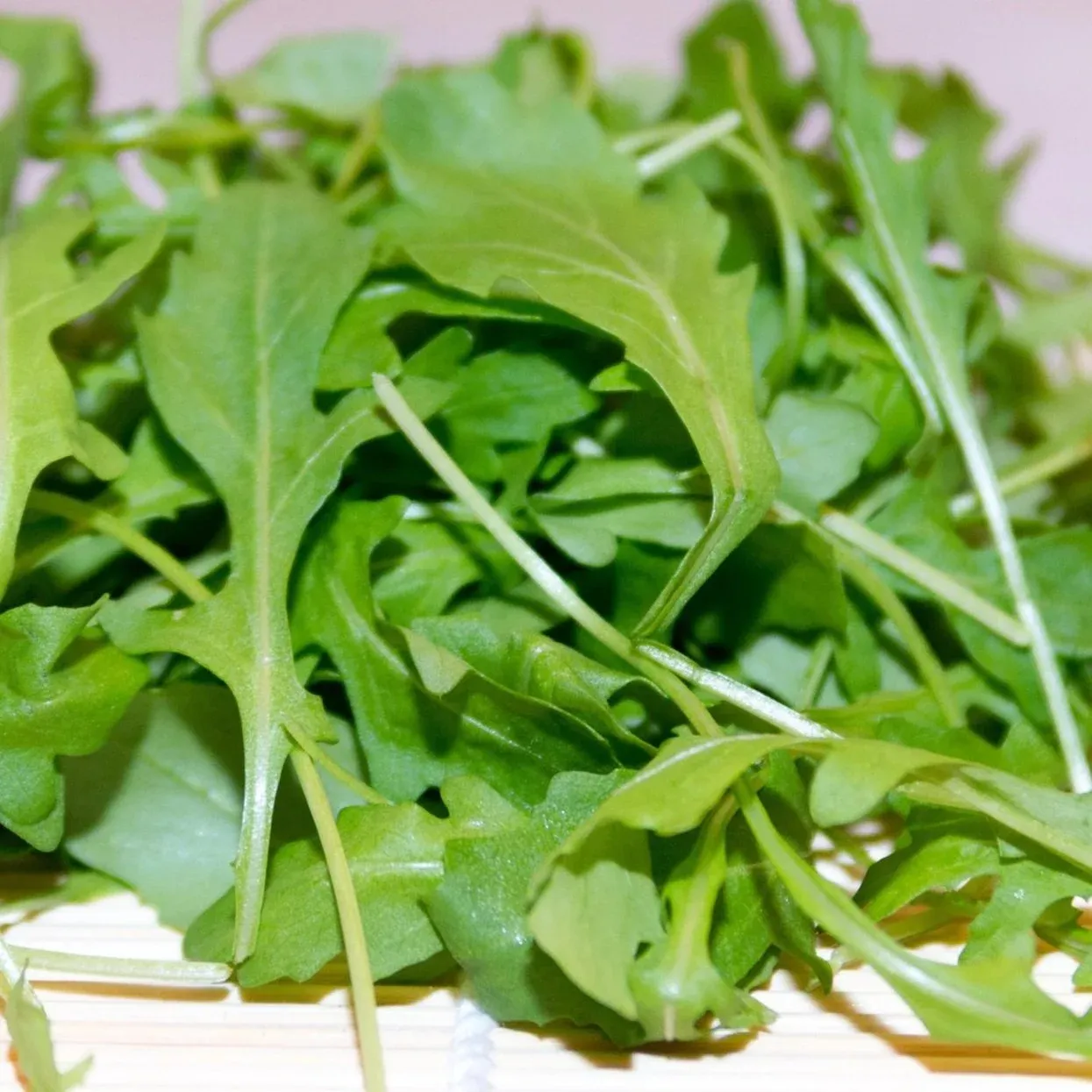 Close-up of a loose pile of fresh arugula leaves and stems on a bamboo mat