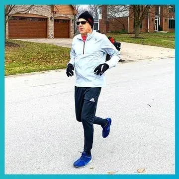 Runner in a knit hat, gloves, light jacket and blue shoes jogging down a suburban street on a gray day