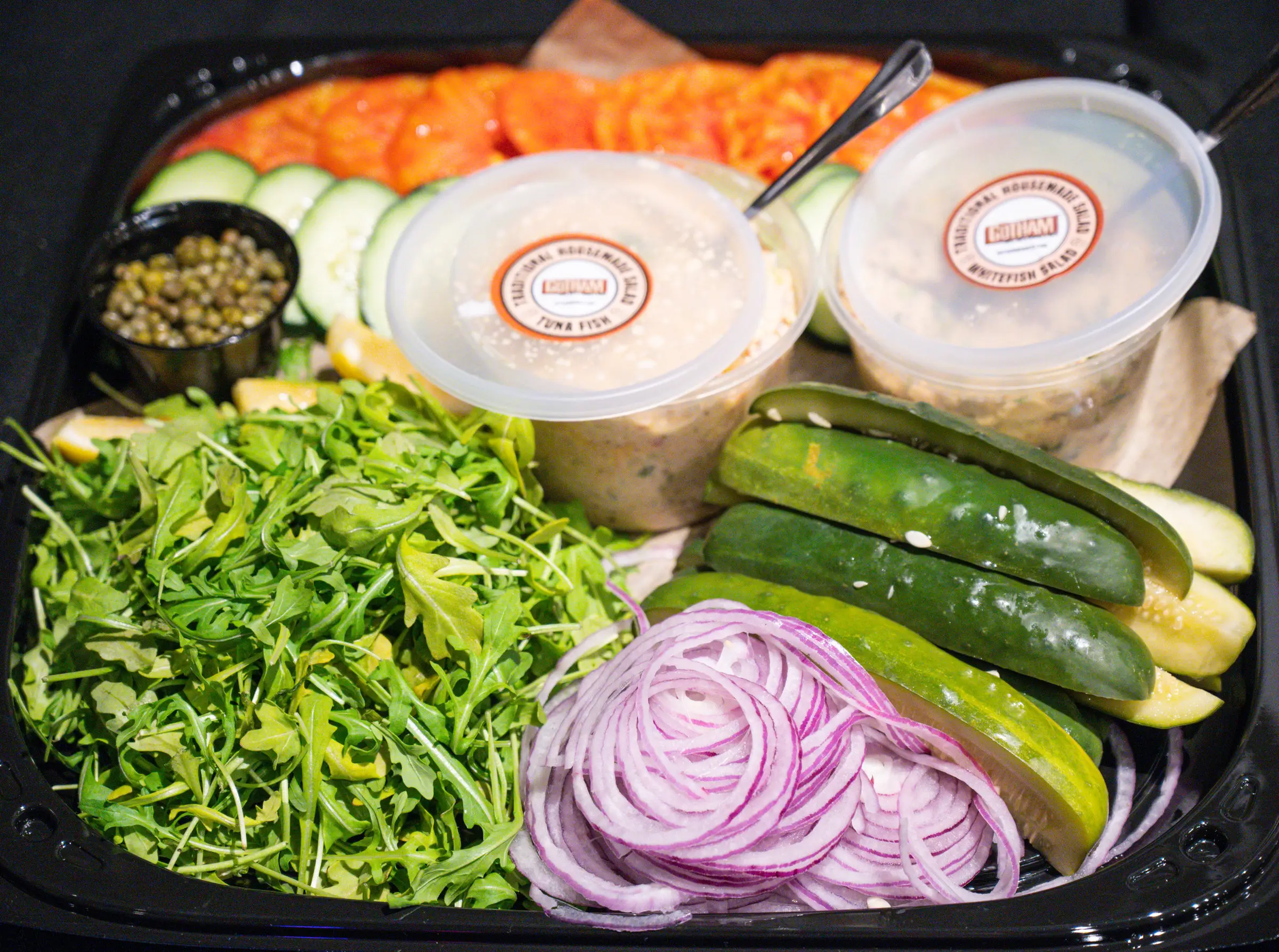 Riverside Park Platter: lox, two tubs of spreads, capers, lemon, arugula, cucumber, pickles and red onion on a black tray