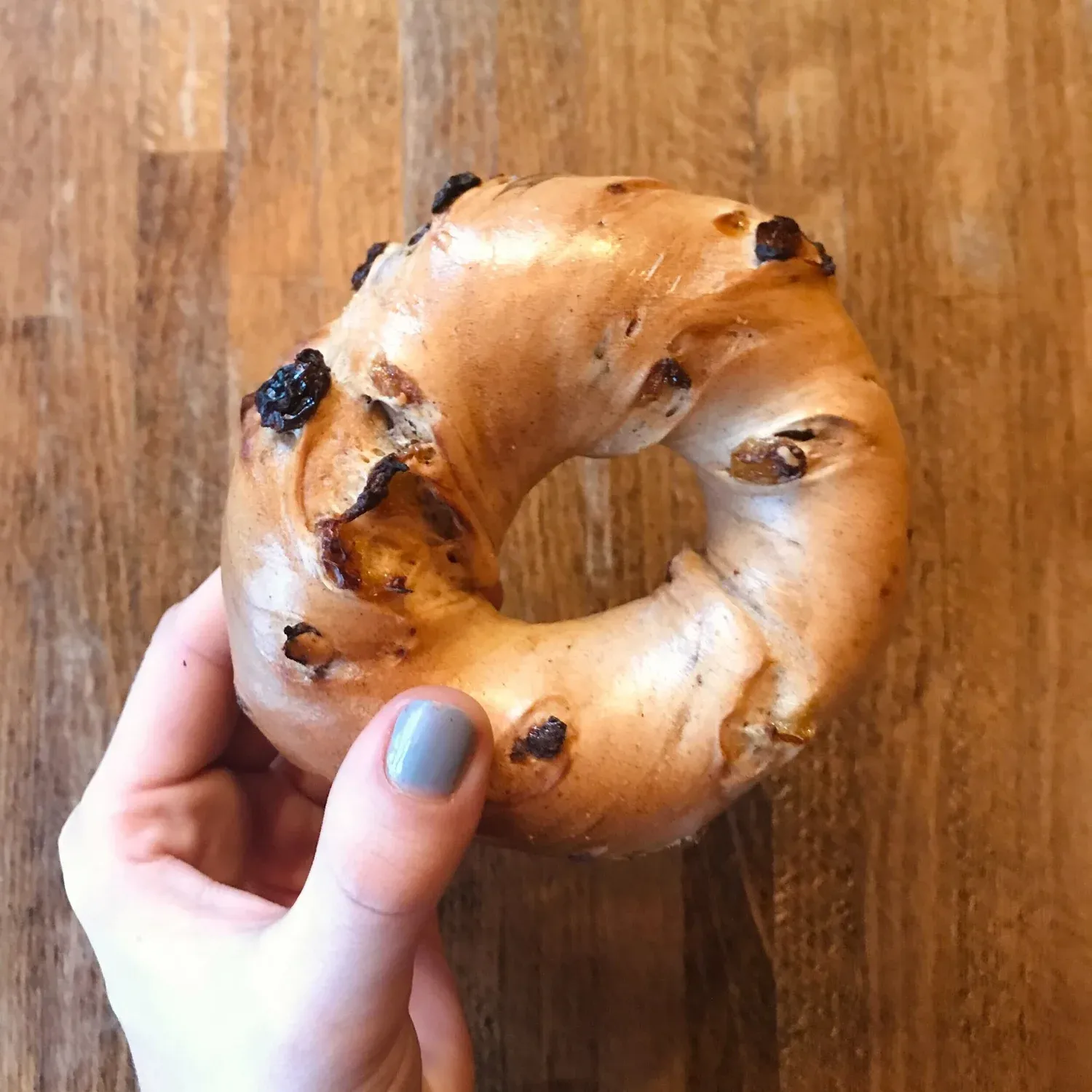 Hand holding a glossy cinnamon raisin bagel over a wooden table