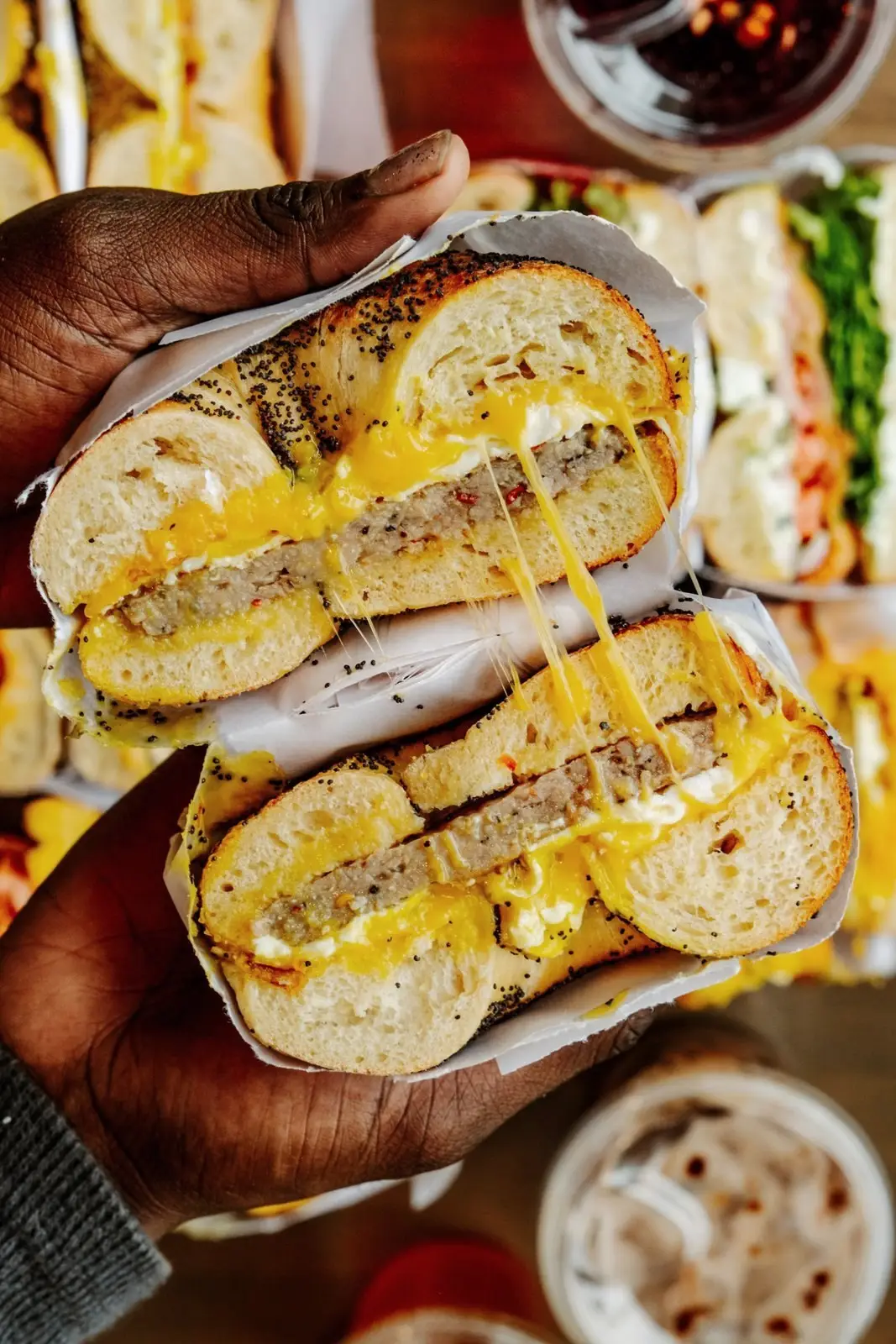 A sausage, egg and cheese on a poppy bagel, cut in half and held up with the cheese pulling between the halves