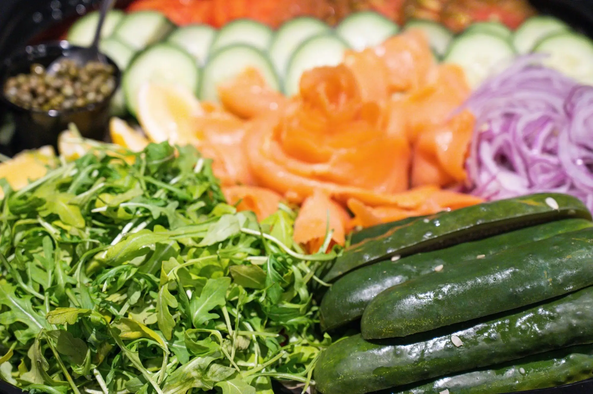 Gotham lox platter: cold-smoked salmon folded into a rose beside arugula, cucumber, red onion, lemon and capers