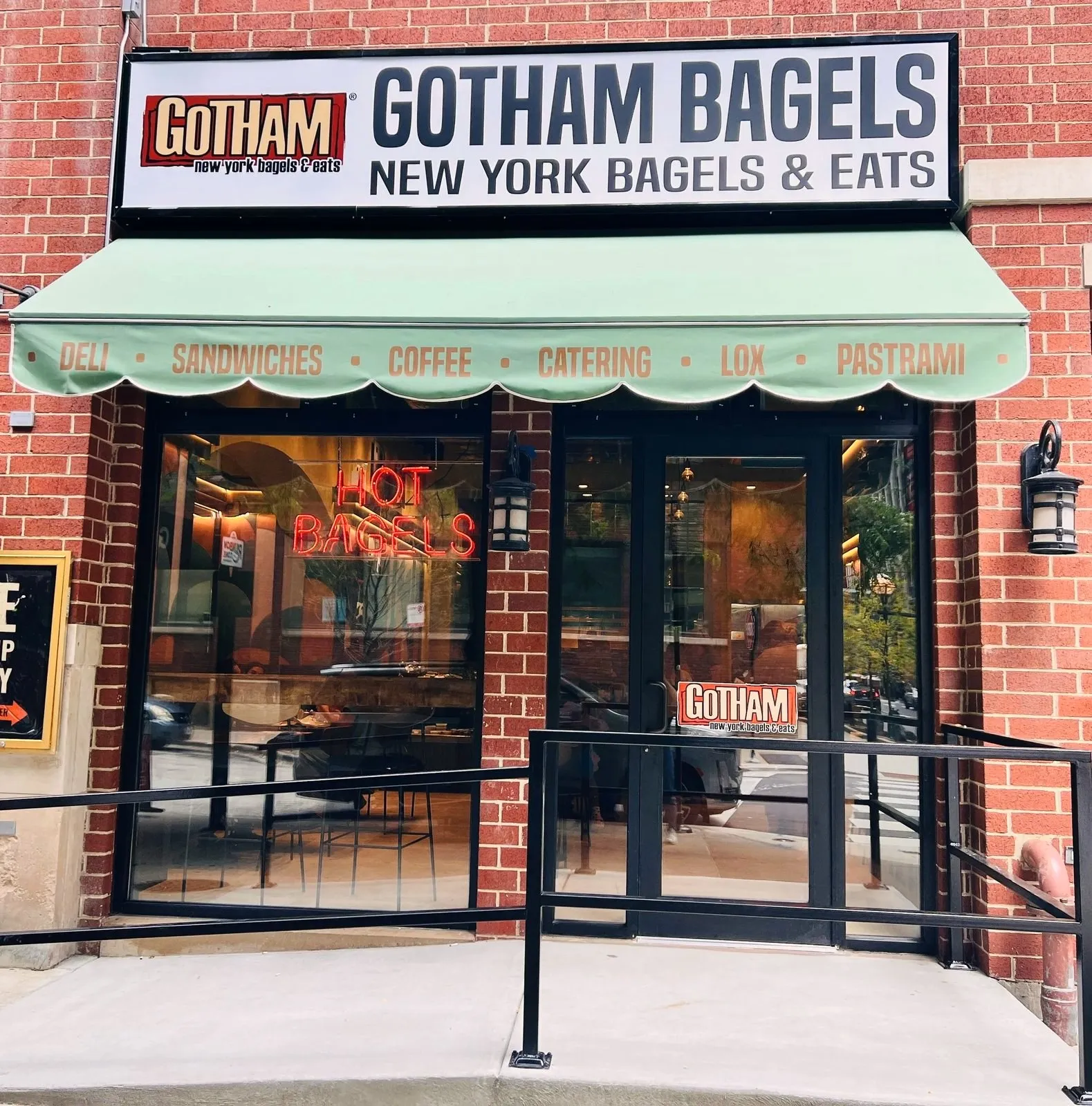 Gotham Bagels Magnificent Mile storefront on E Superior St, with a green awning and Hot Bagels neon in the window