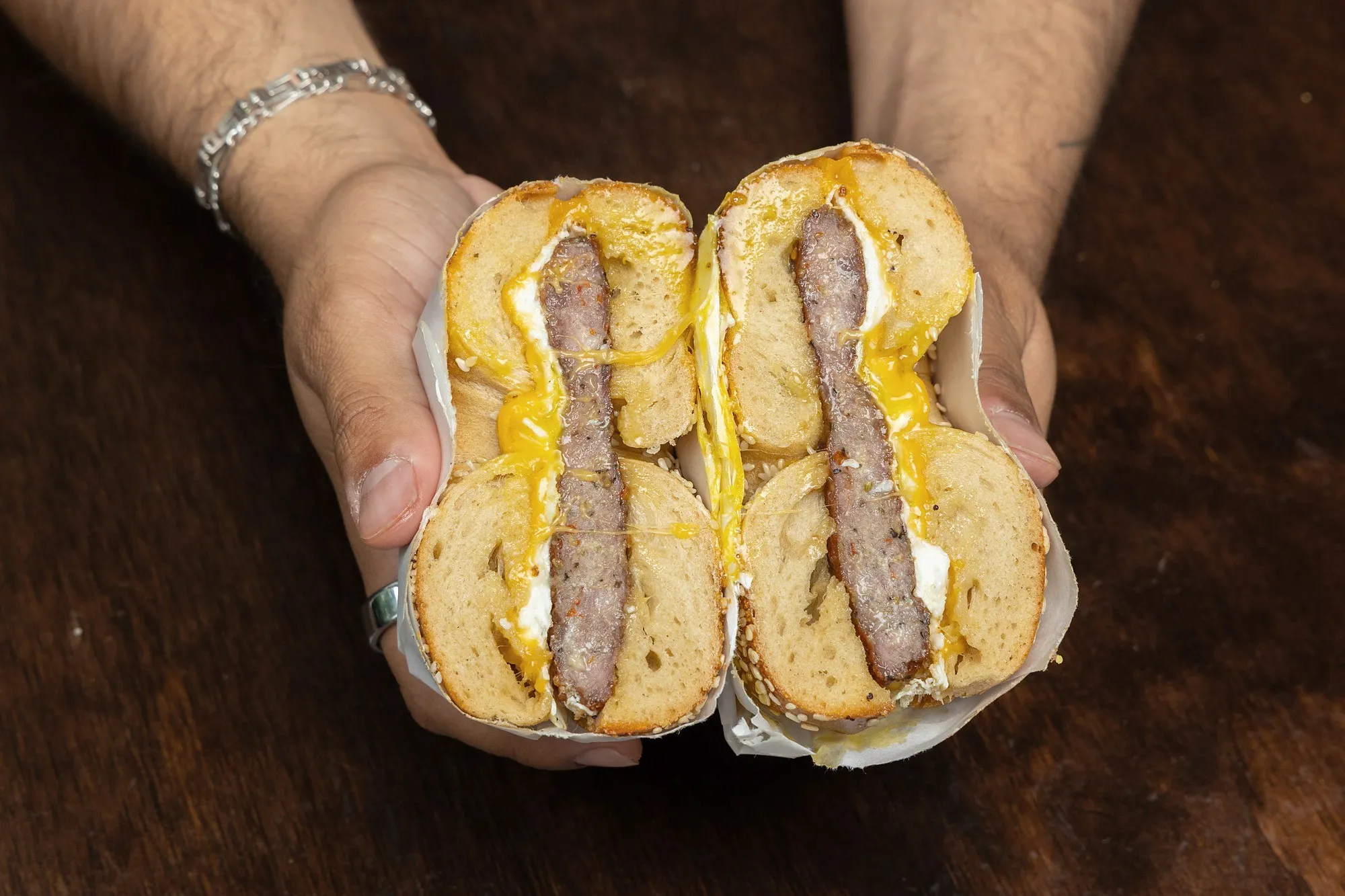 A Spicy Sausage, Egg & Cheddar on a sesame bagel, cut in half and held up in two hands