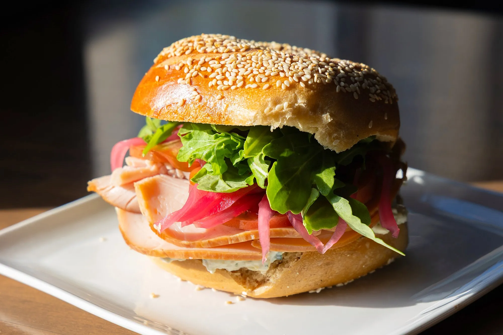 A turkey sandwich with arugula and pickled red onion on a sesame bagel