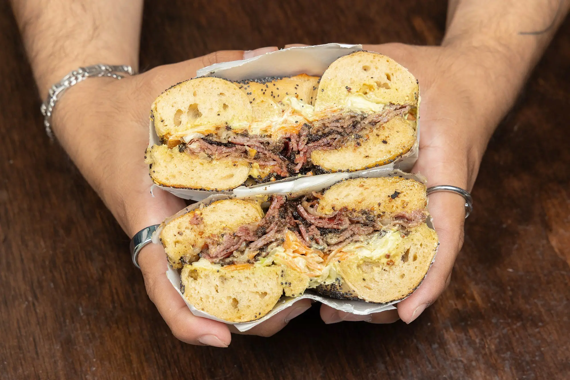 Williamsburg hot pastrami bagel sandwich held in two hands