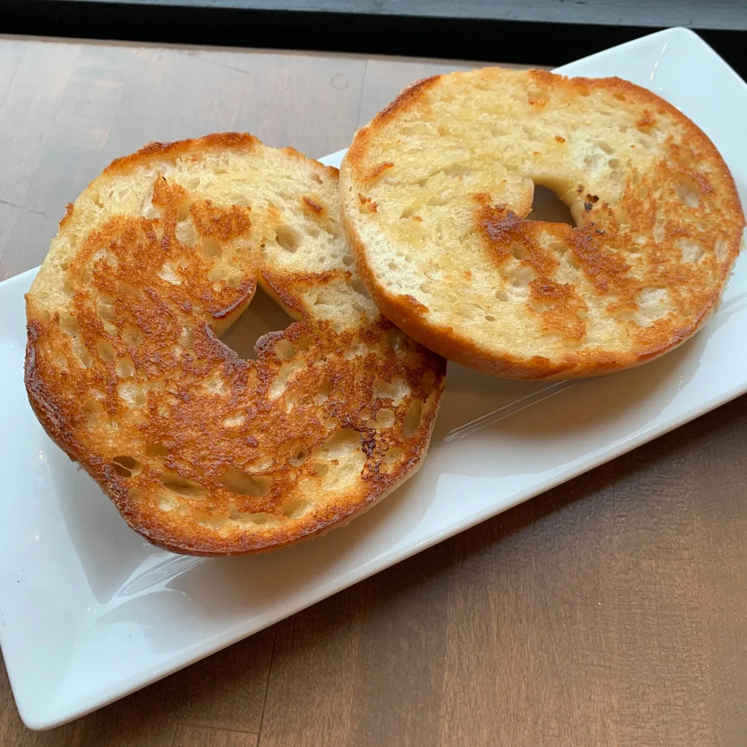 Two toasted bagel halves with golden-brown griddle marks on a white rectangular plate