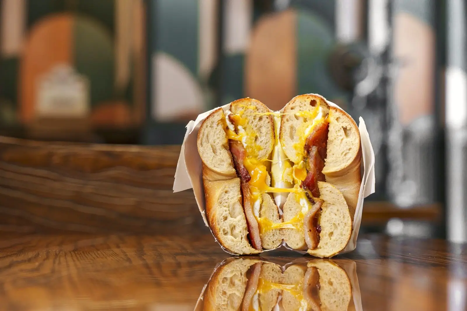 A Gotham bagel sandwich cut in half on a wooden table, melted cheese and giardiniera peppers showing in the cross-section