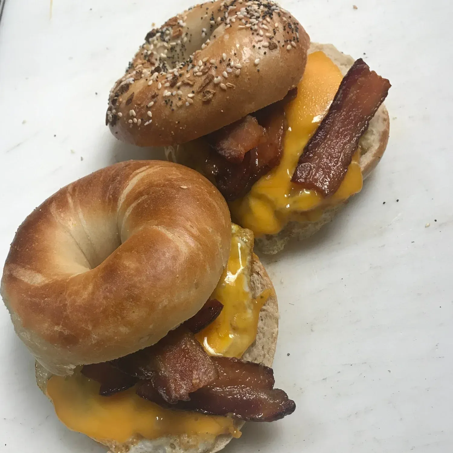 Two open bacon, egg and melted cheddar bagel sandwiches, one on an everything bagel and one on plain